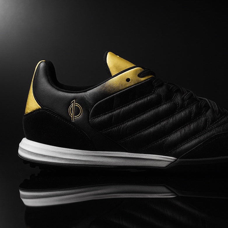 Black sneaker with gold accents on a reflective black surface