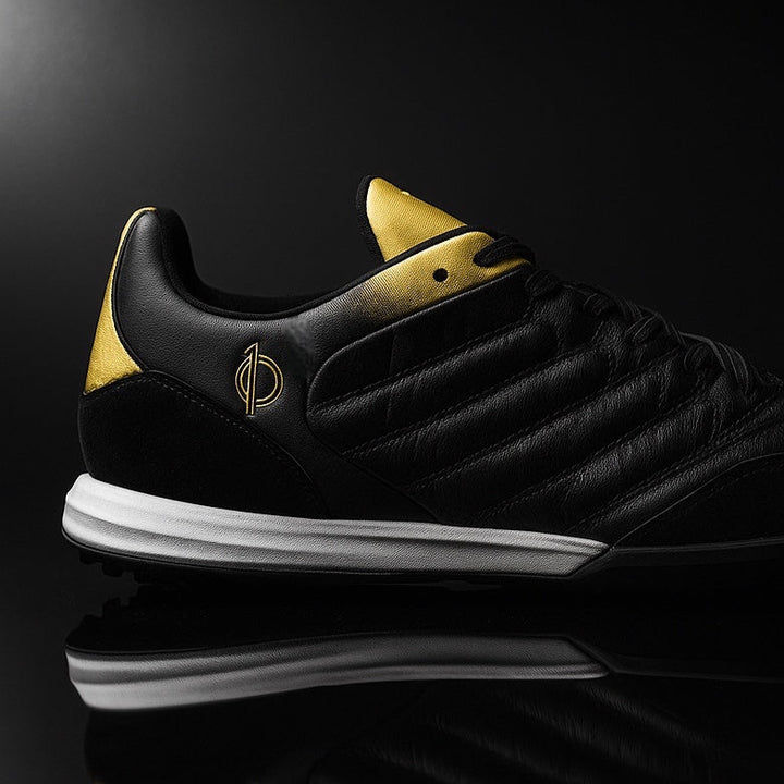 Black sneaker with gold accents on a reflective black surface